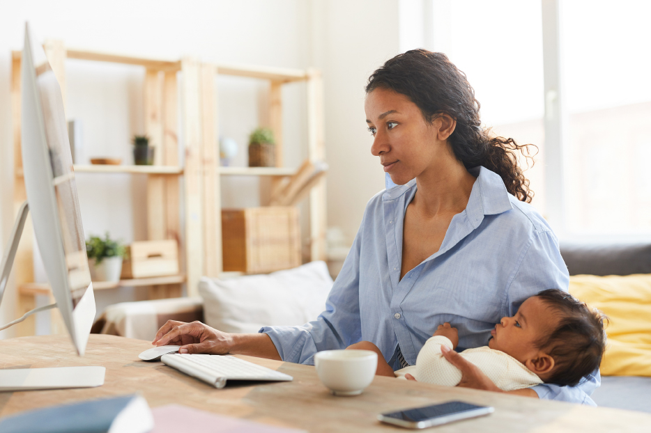 Woman at computer holding child.